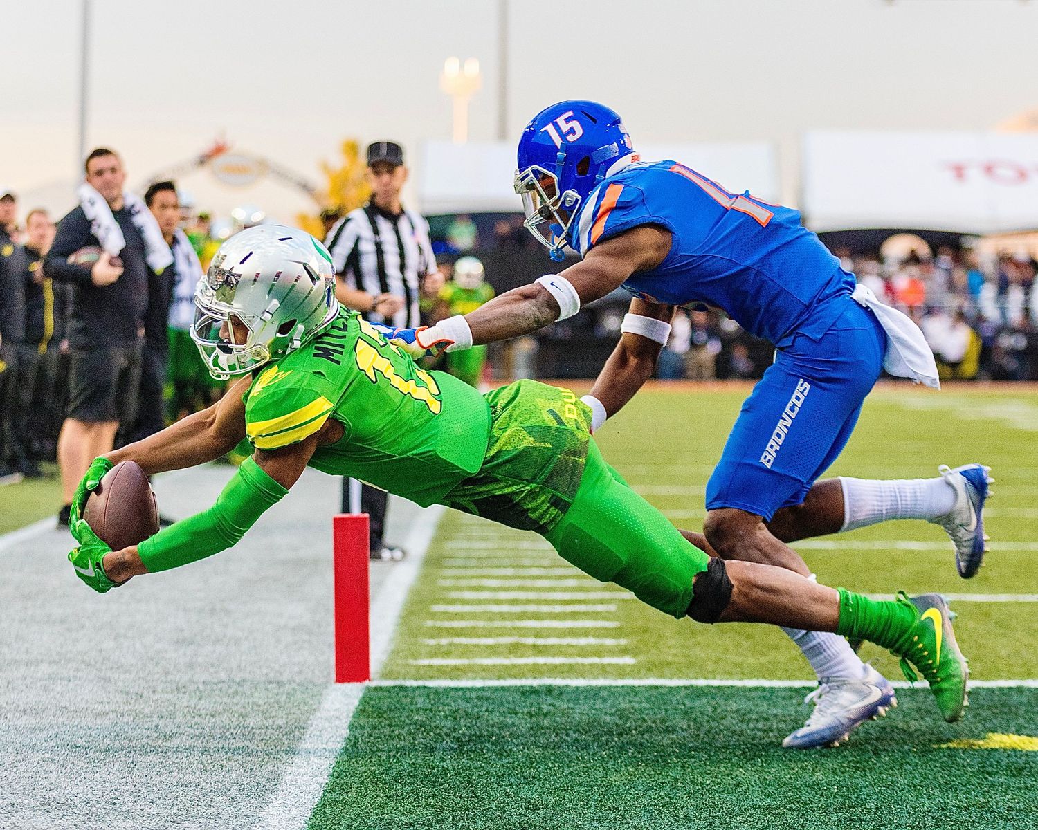 Football players from opposing teams diving towards the goal line during intense play.