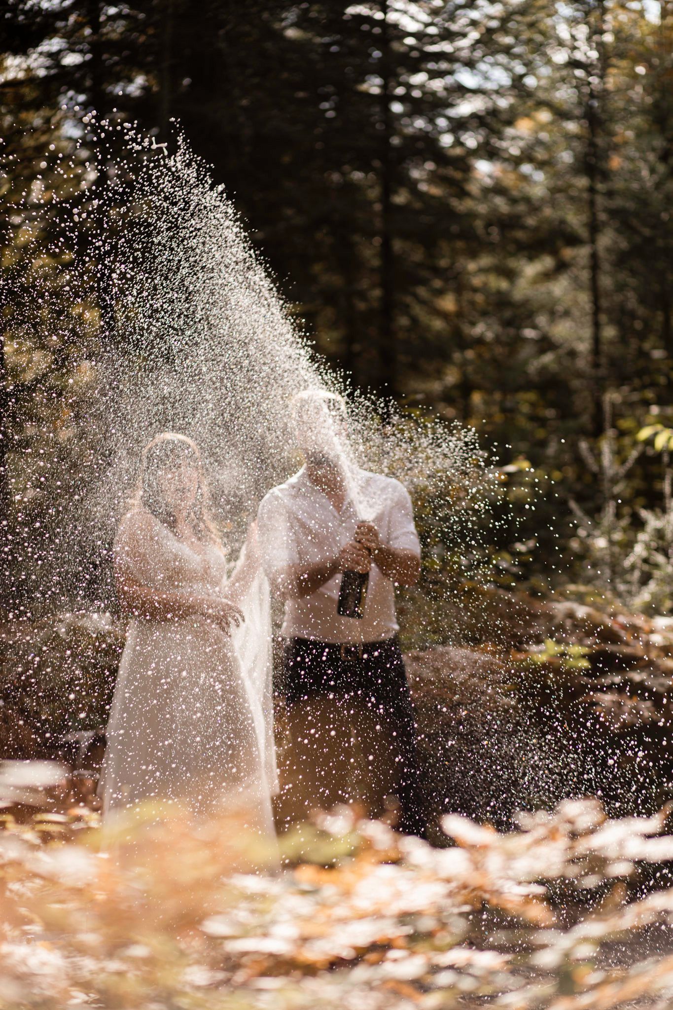 couple celebrates vows with spraying champagne in the sunlight, at their mountain treehouse elopement mont tremblant quebec canada