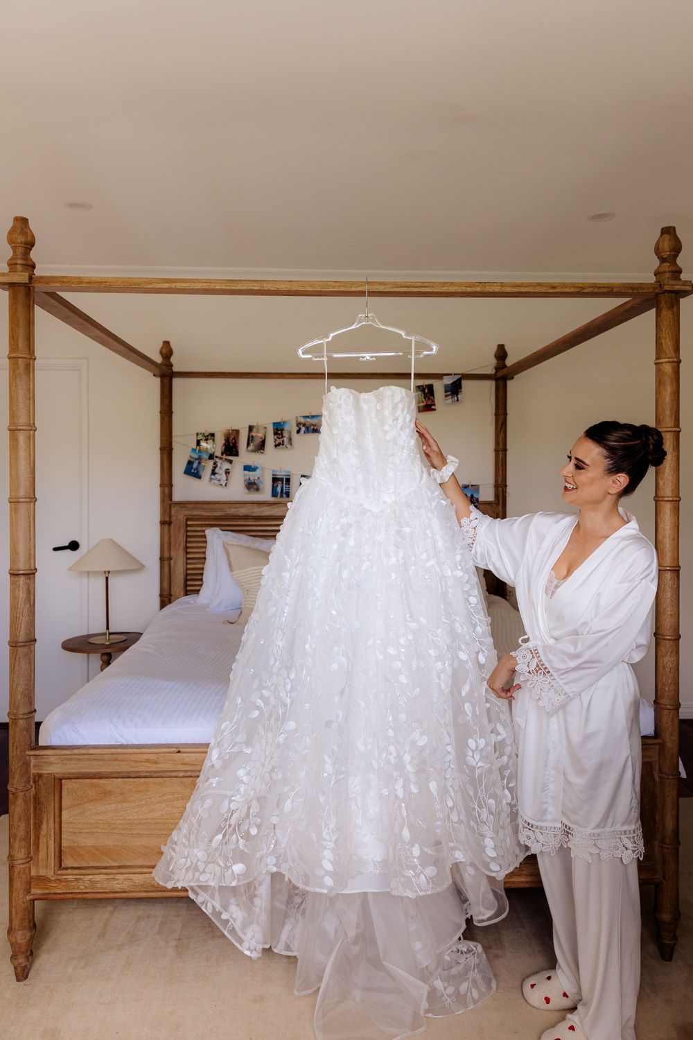 A white lace wedding dress hangs from a wooden four-poster bed frame.