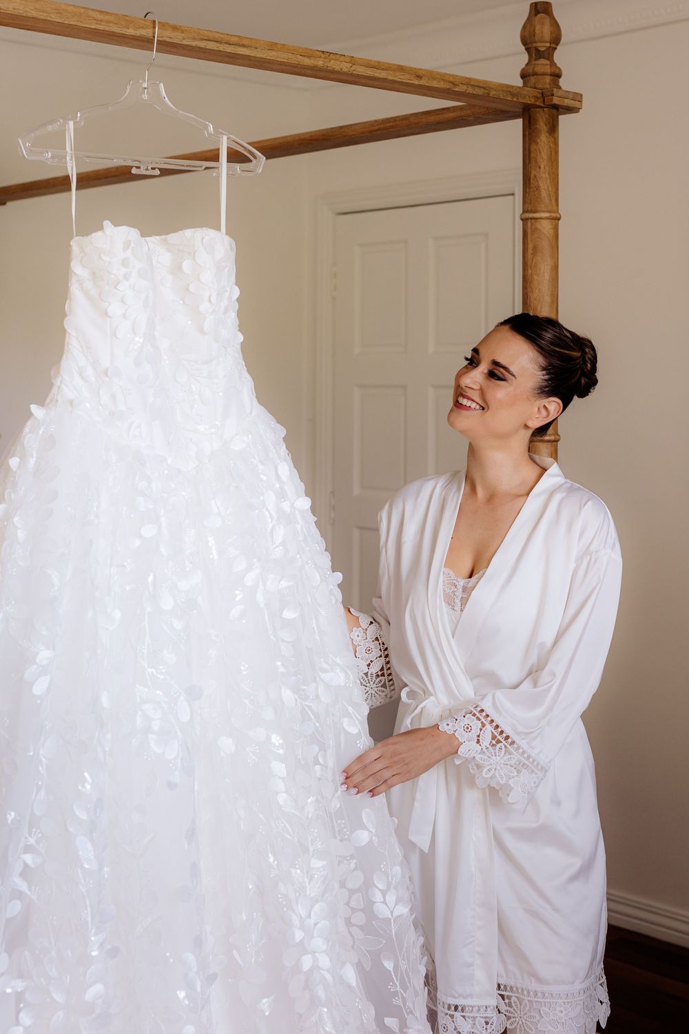 White wedding dress hanging on wooden four-poster bed frame while getting ready.