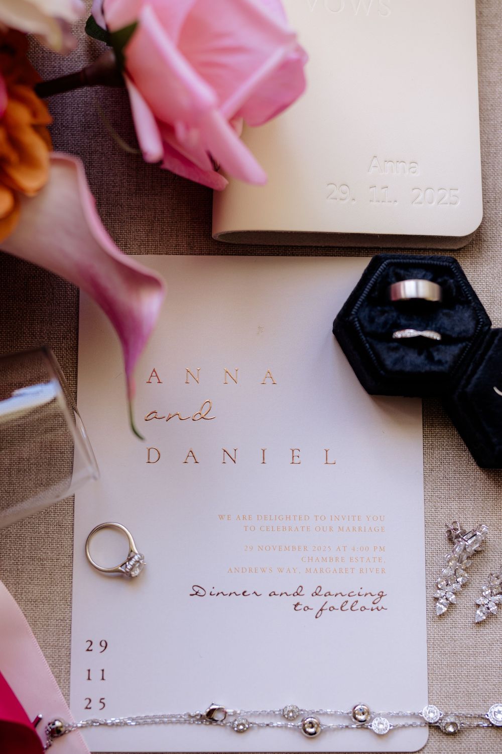 Wedding invitation details with rings, jewelry and pink accents laid out on a neutral background.