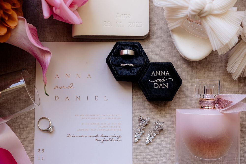 Wedding details including invitations, rings, and pink accessories arranged on a light surface.