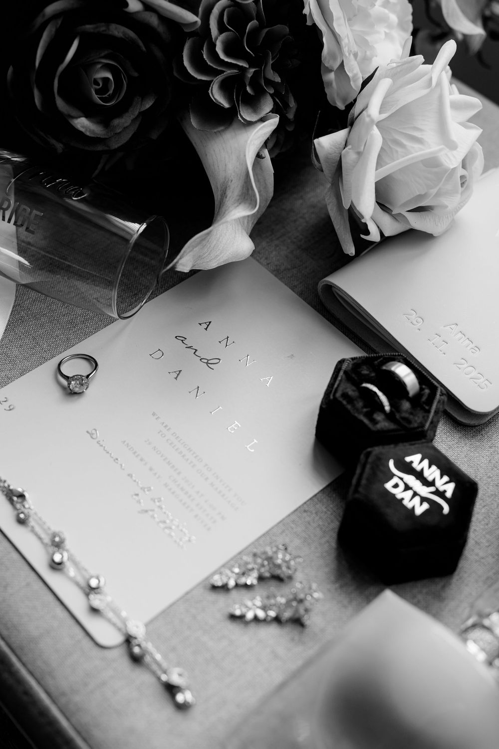 Black and white detail shot of wedding rings, flowers and handwritten notes on paper.