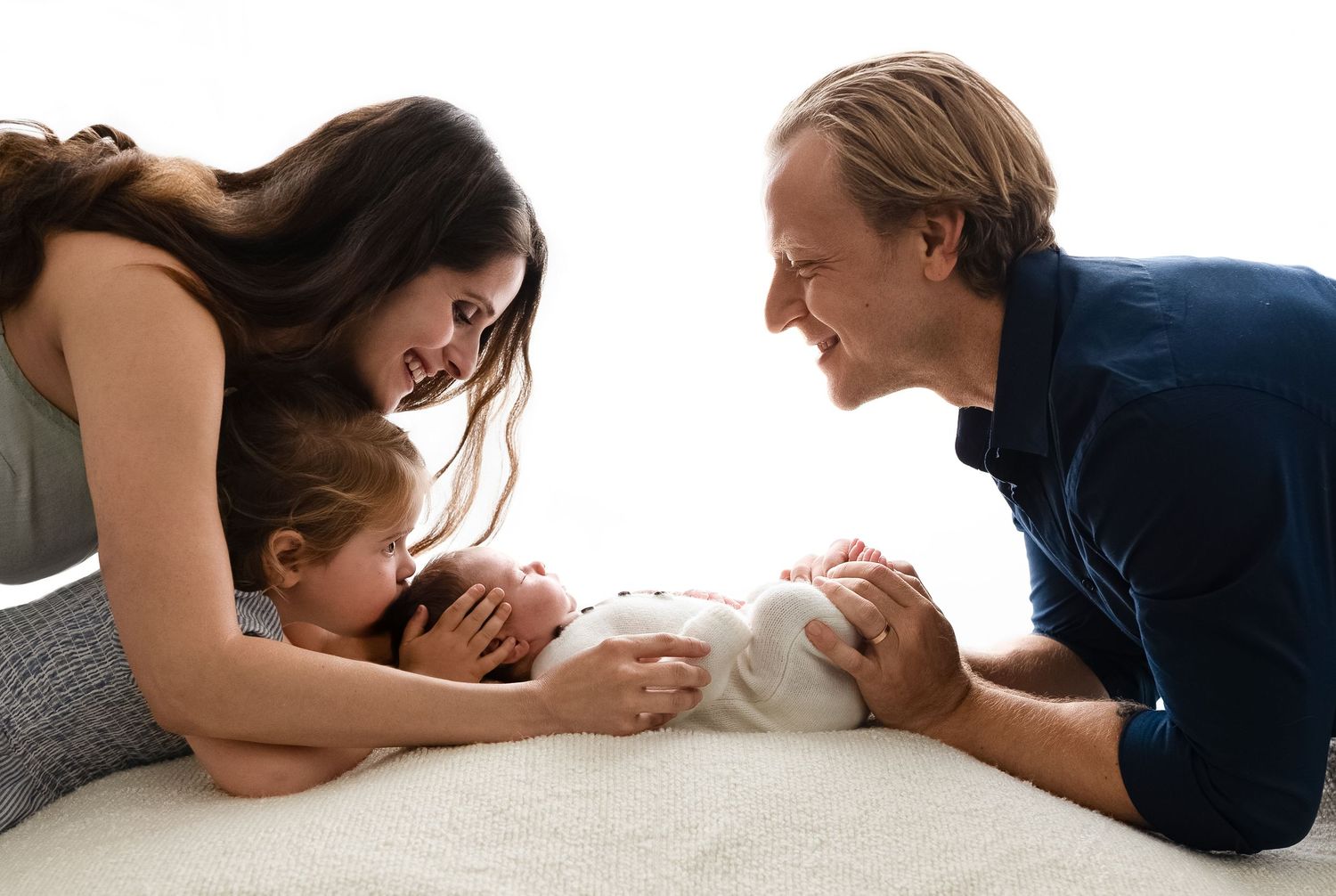 Backlit image of parents big sister leaning over her newborn sister, captured by Charlottesville baby and family photographer.