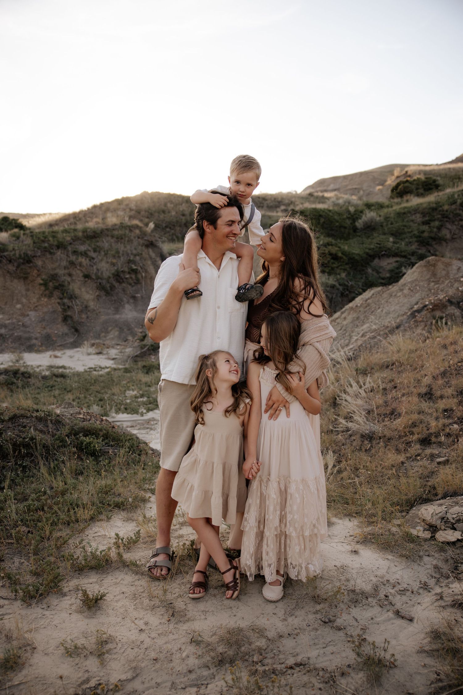 Family wearing neutral tones poses together on a desert hillside at sunset for a portrait session.