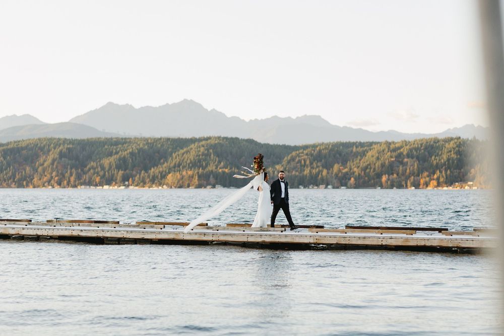 Bride and groom walking on a lakeside dock with mountain backdrop on their wedding day.