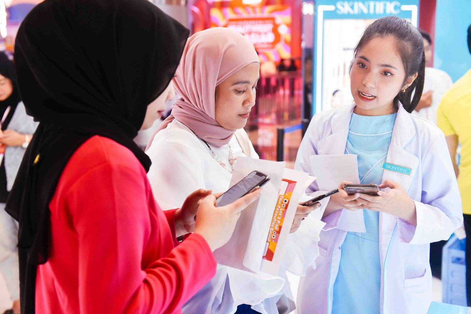 Students in white lab coats and hijabs work together in a laboratory setting with bright lighting and equipment.