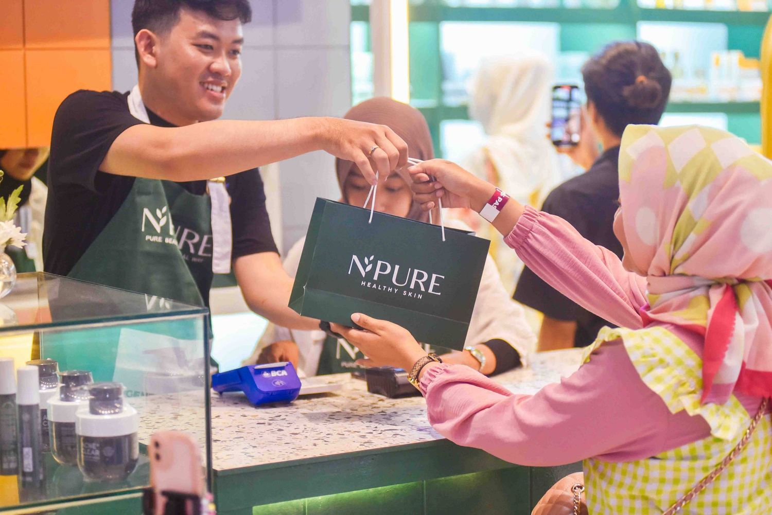 People prepare beverages at a drink station with colorful ingredients and cups arranged on the counter.