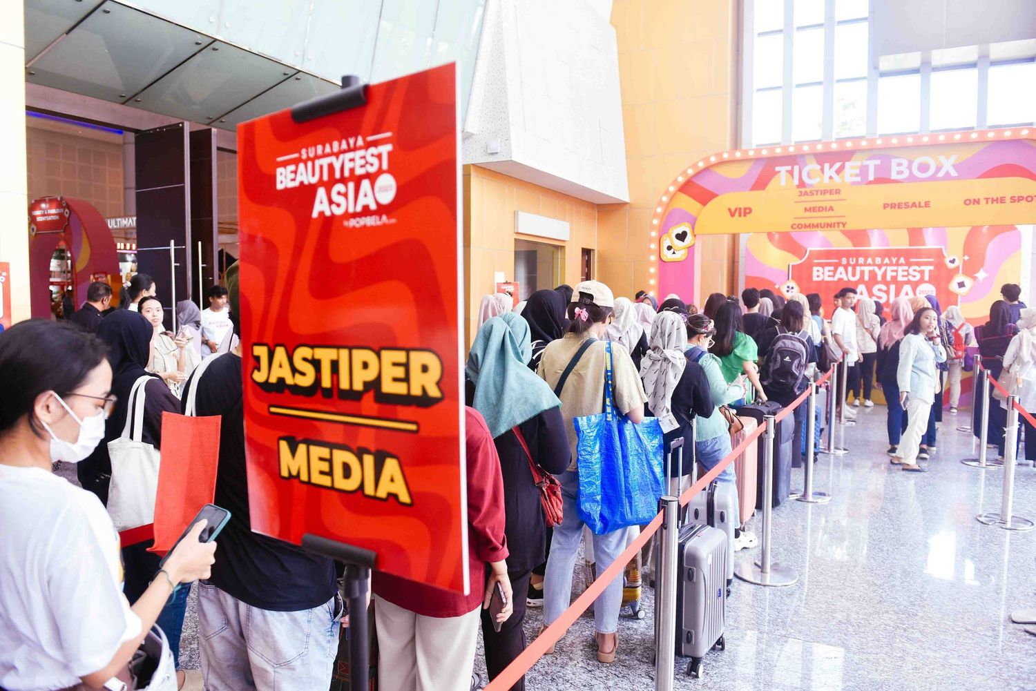 Long lines of people waiting near red signage in a shopping mall hallway.