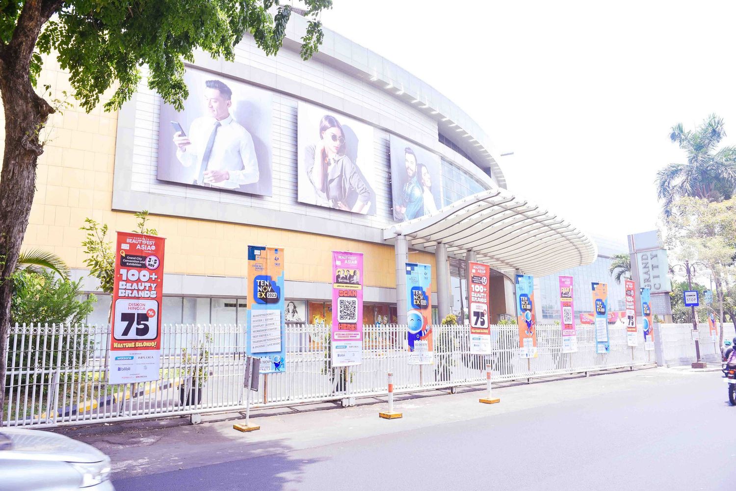 Panoramic view of a modern shopping center exterior with green trees and signage along the storefront.