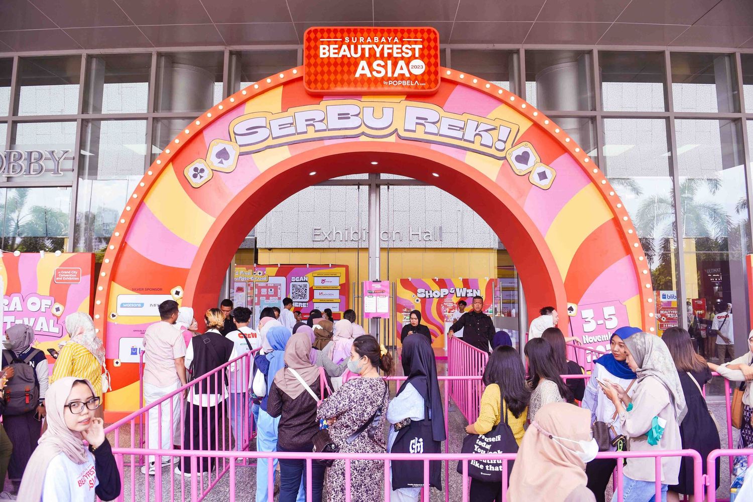 Crowd of people gathering under a colorful orange and pink arch entrance at an Asian food festival event.