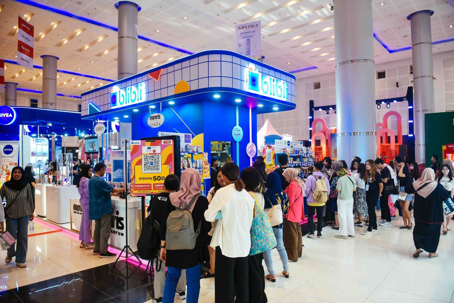 A crowd of people gathering in a modern shopping mall with blue LED lighting and white columns.