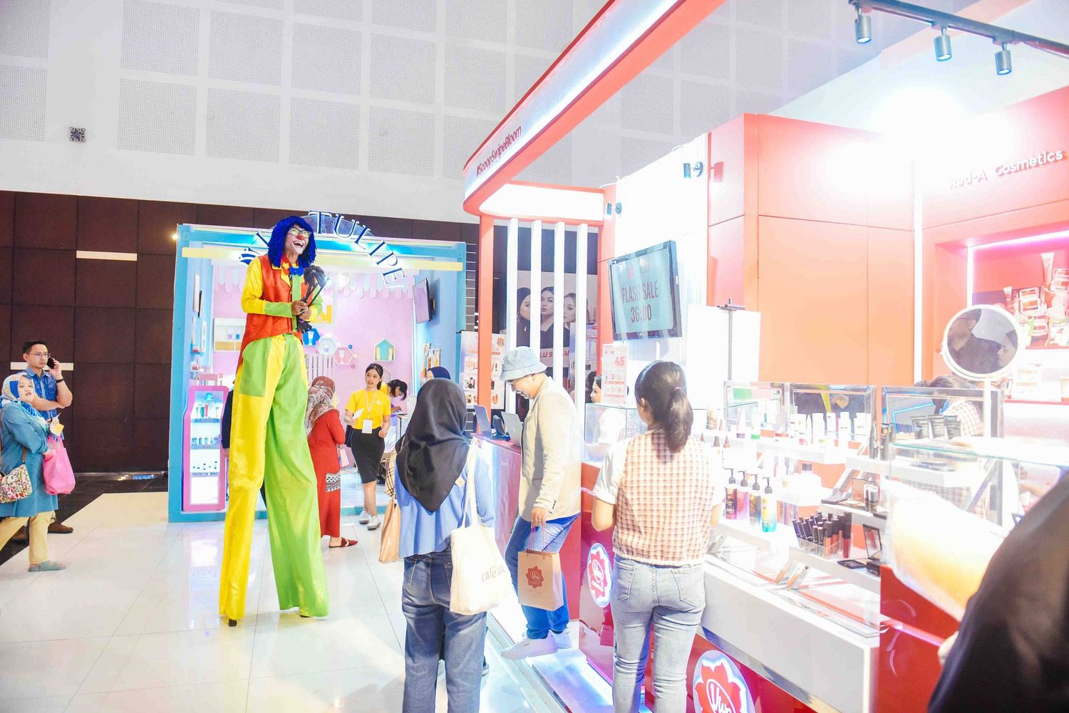 A performer on stilts wearing bright yellow pants entertains children at an indoor venue with colorful lighting.