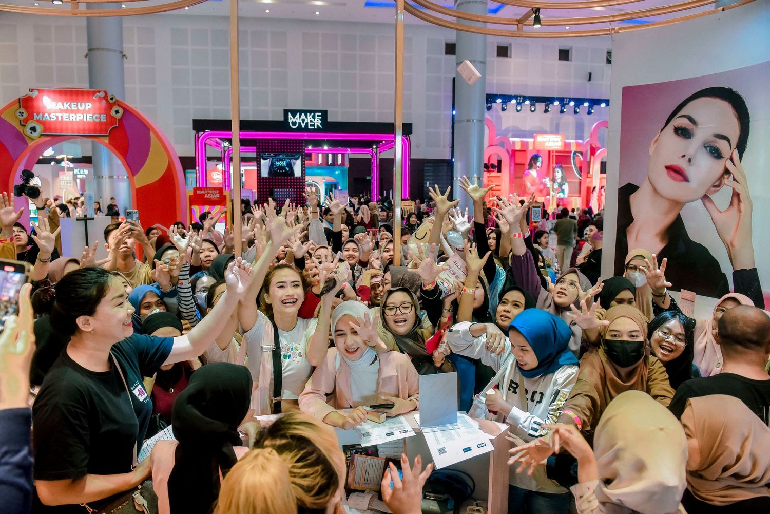A lively crowd gathers in a brightly lit venue with pink and blue lighting for a social event or celebration.