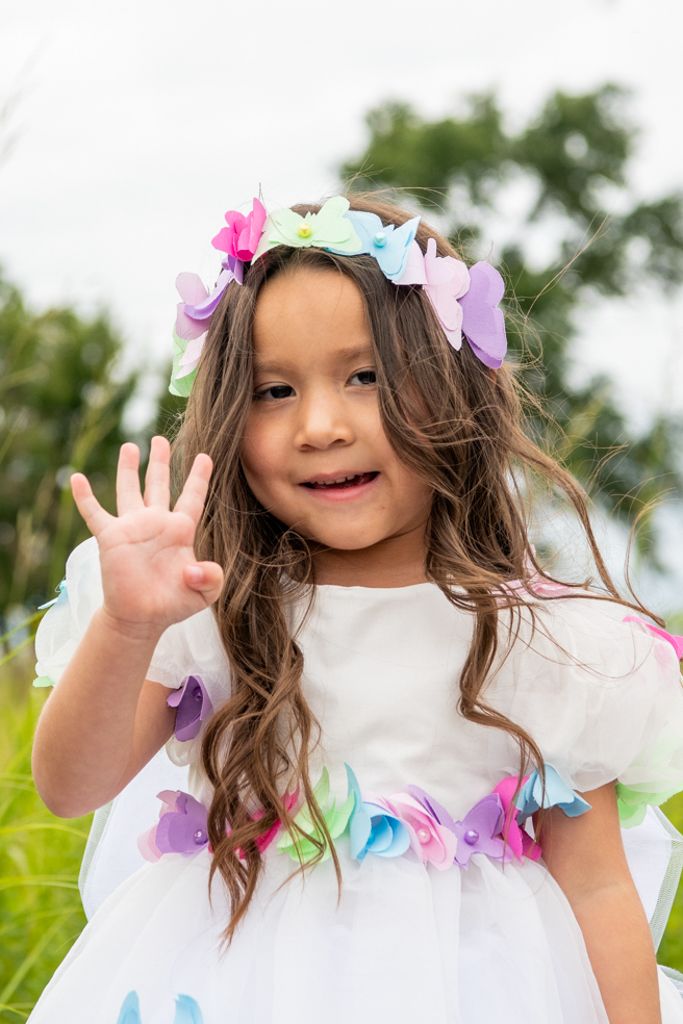 Colorful pink and blue balloons decorate an outdoor celebration with a floral crown and white dress.