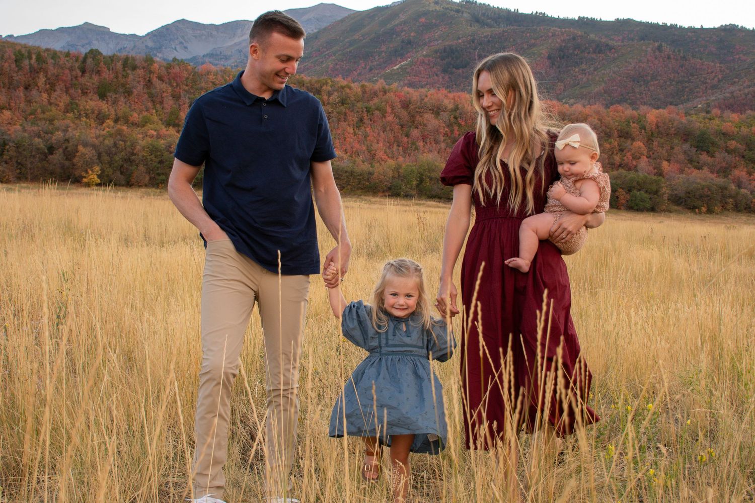 A family walks through a golden autumn field with mountains in the background during sunset.