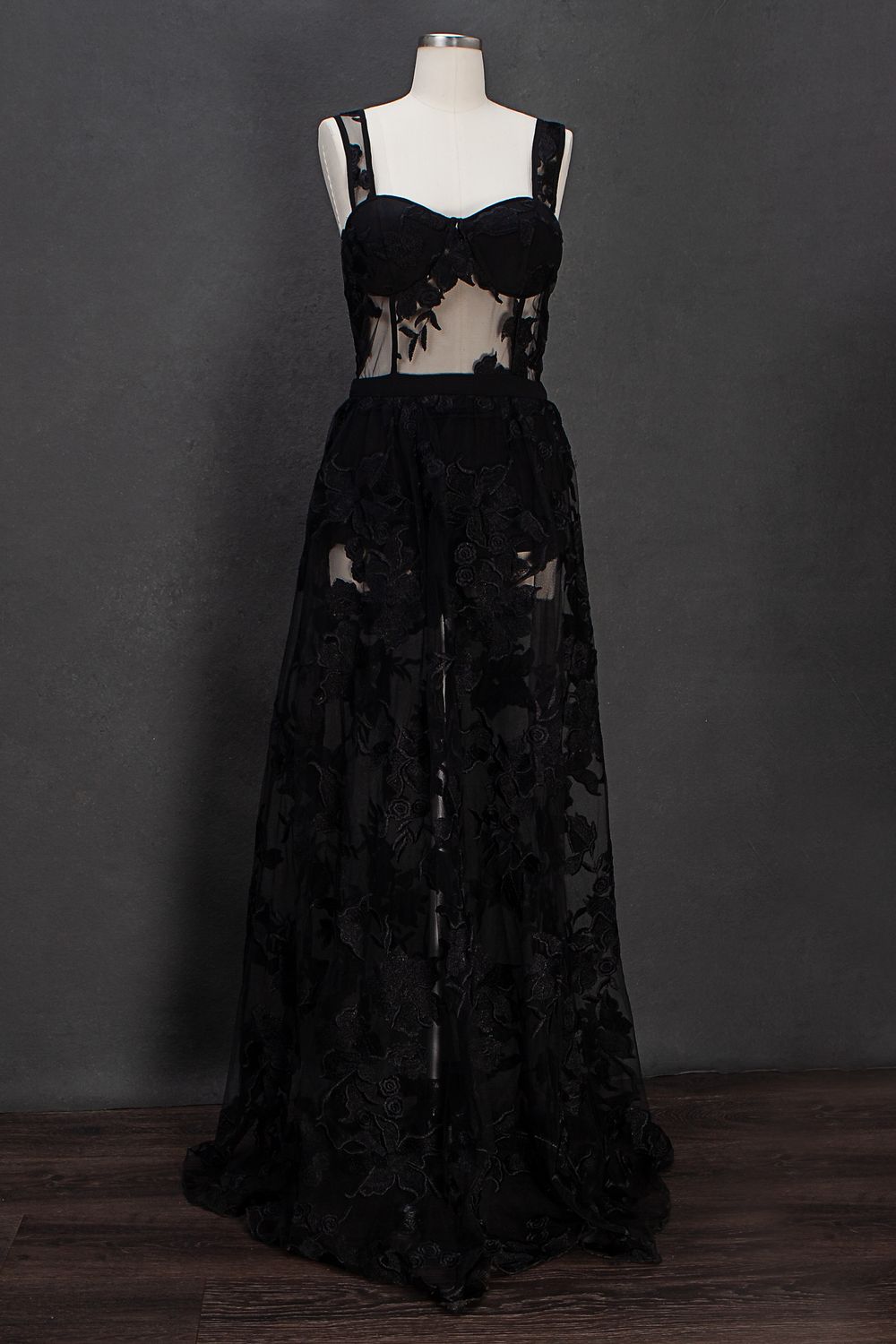 A black lace formal dress with spaghetti straps and floral details displayed on a mannequin against a dark background.
