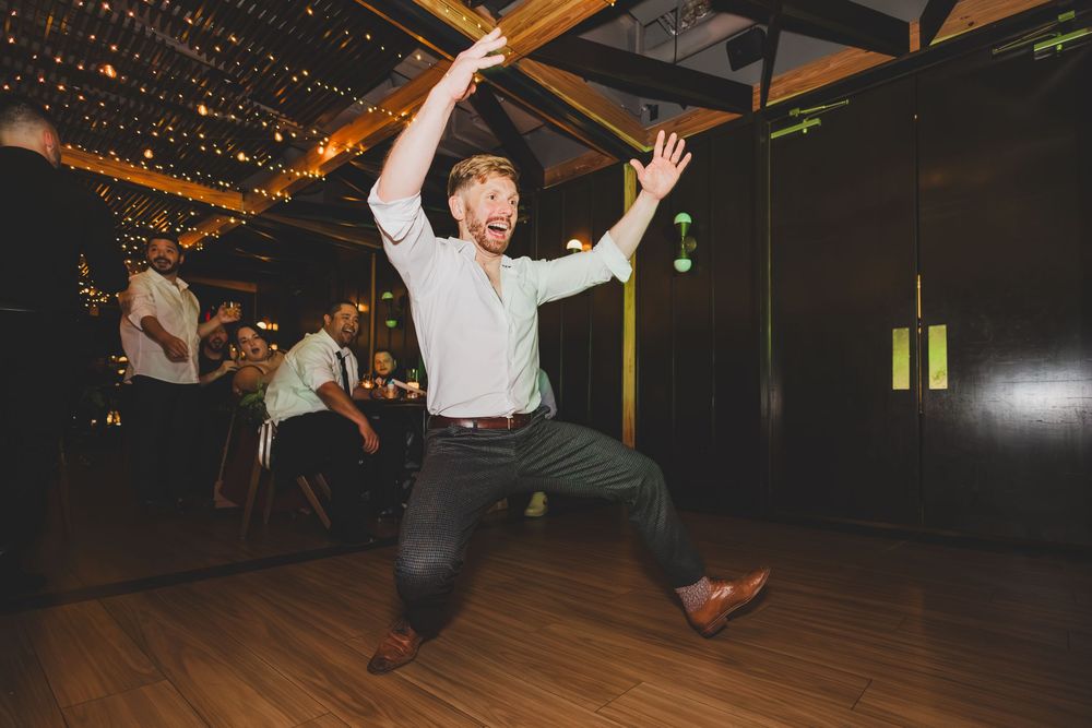 People dancing and jumping energetically at a dimly lit party venue with string lights overhead.