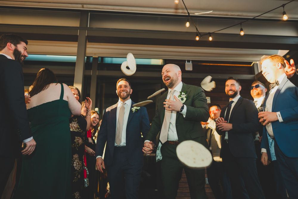Wedding guests throw paper plates in celebration during a fun reception moment at an indoor venue.
