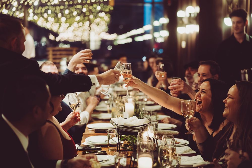 People enjoying drinks and conversation at a dimly lit restaurant bar with festive string lights overhead.