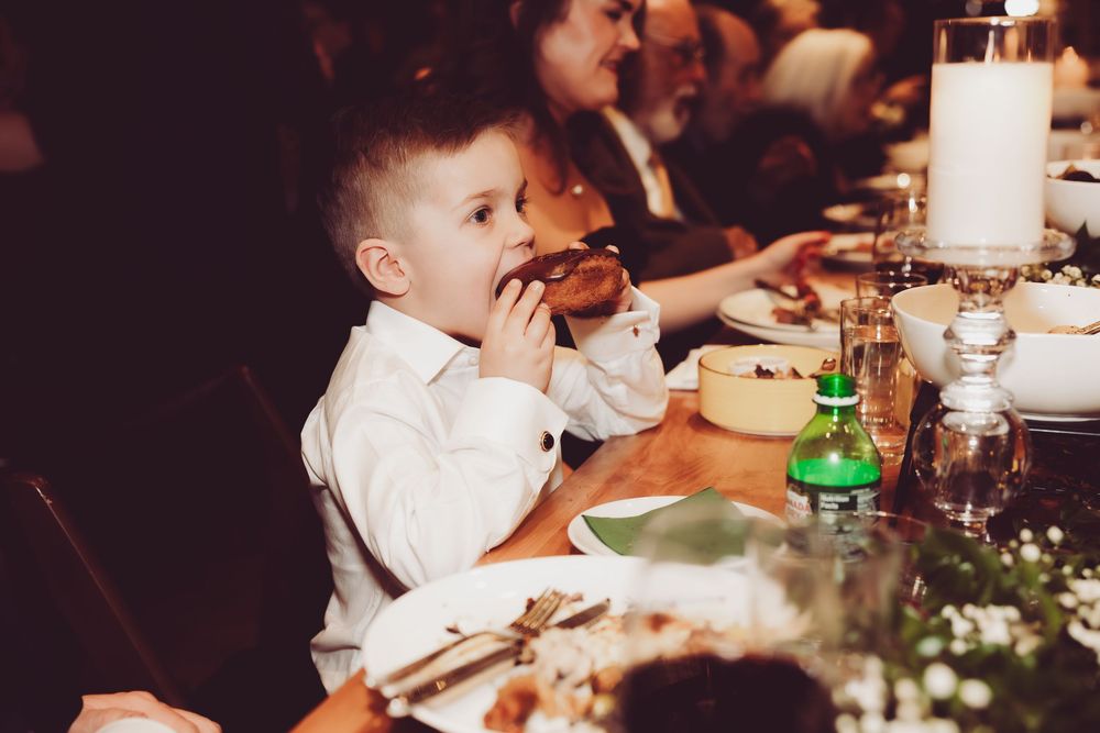 Young child in white shirt enjoying a meal at a formal dinner table with drinks and decorative settings.