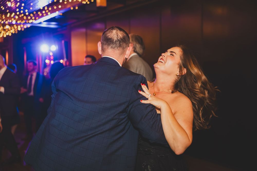 Couple dancing together at a wedding reception with string lights and colorful lighting in the background.