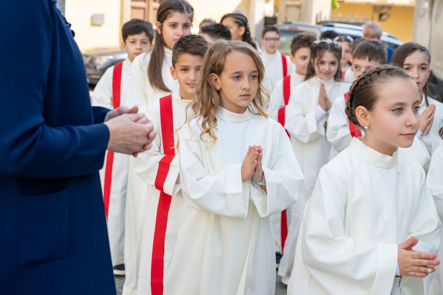 Group of choir members wearing white robes with red stoles walking in procession.