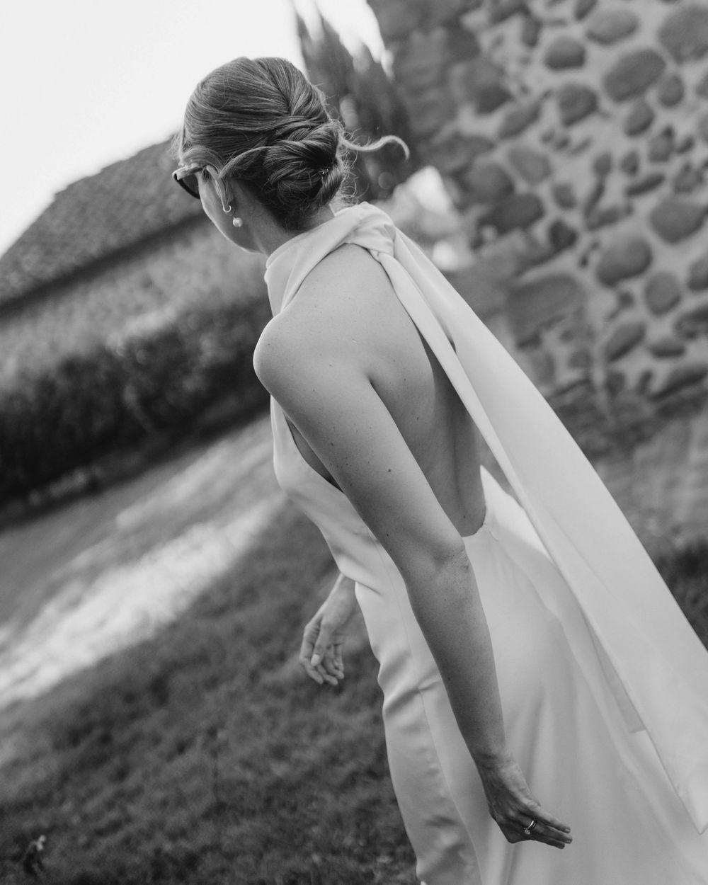 A bride in a flowing white dress walks along a stone wall in black and white photography.