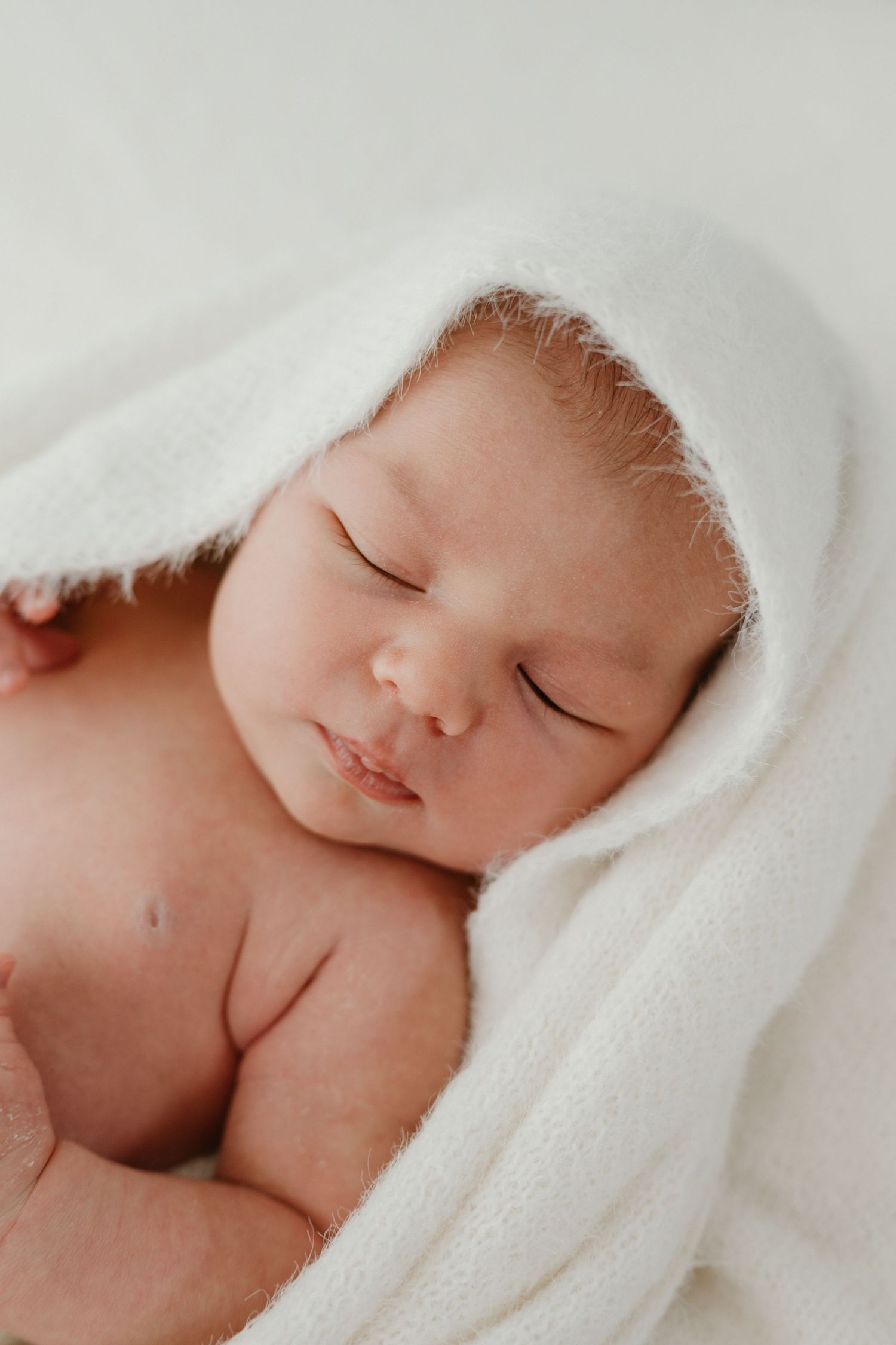 Peaceful newborn baby sleeping wrapped in a soft white hooded towel blanket.