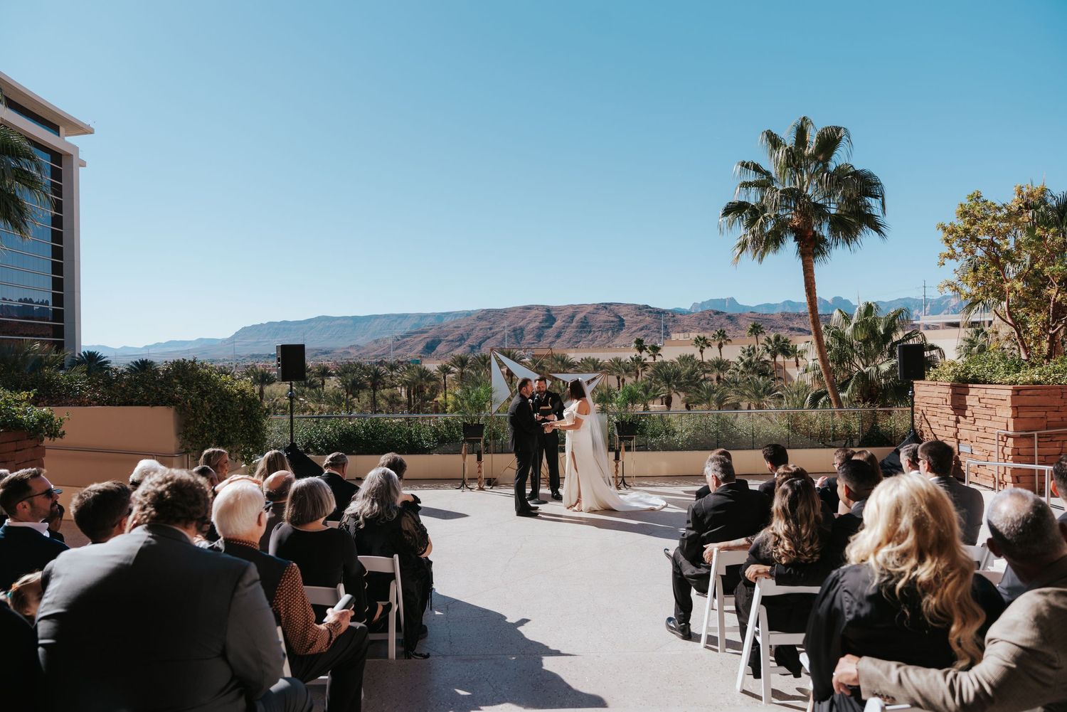 Panoramic view of people gathering outdoors at a desert venue with mountains and palm trees in the background.