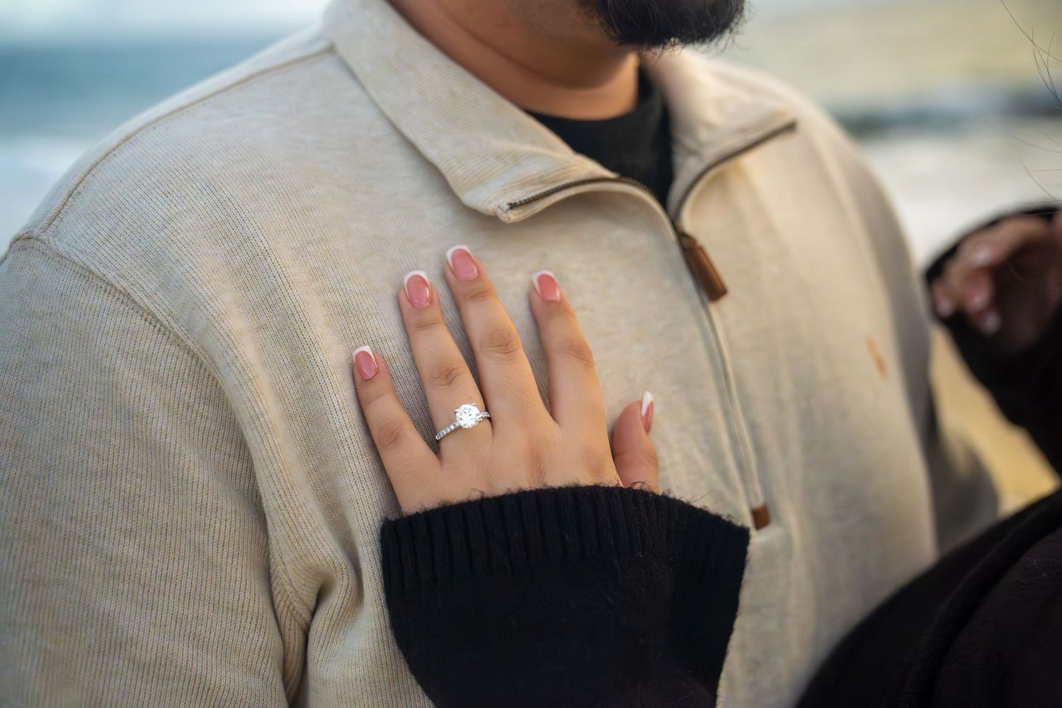 Close-up of hands showing a sparkling diamond engagement ring in natural lighting.
