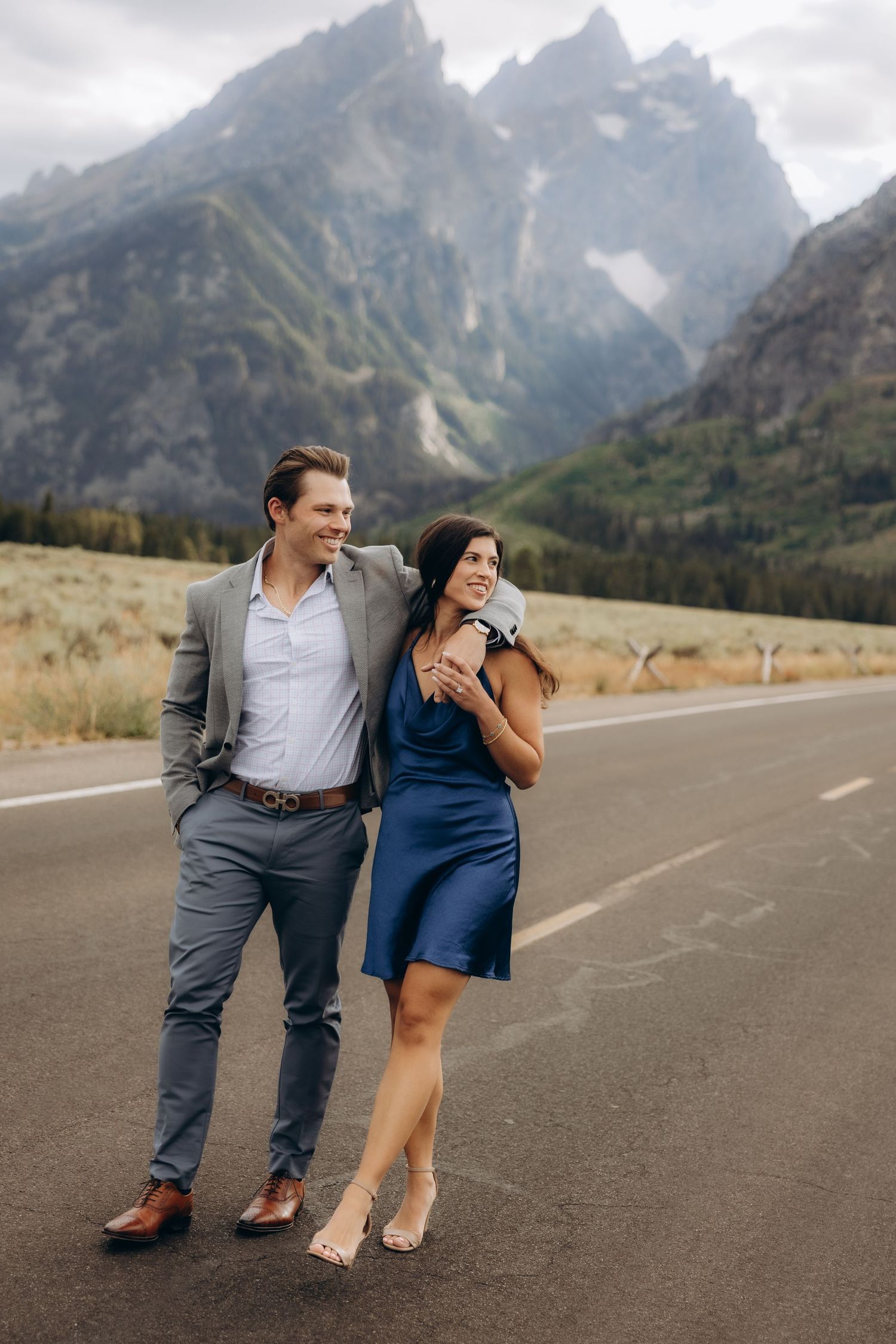 A couple enjoying a romantic moment on a mountain road with majestic Grand Teton peaks in the background.