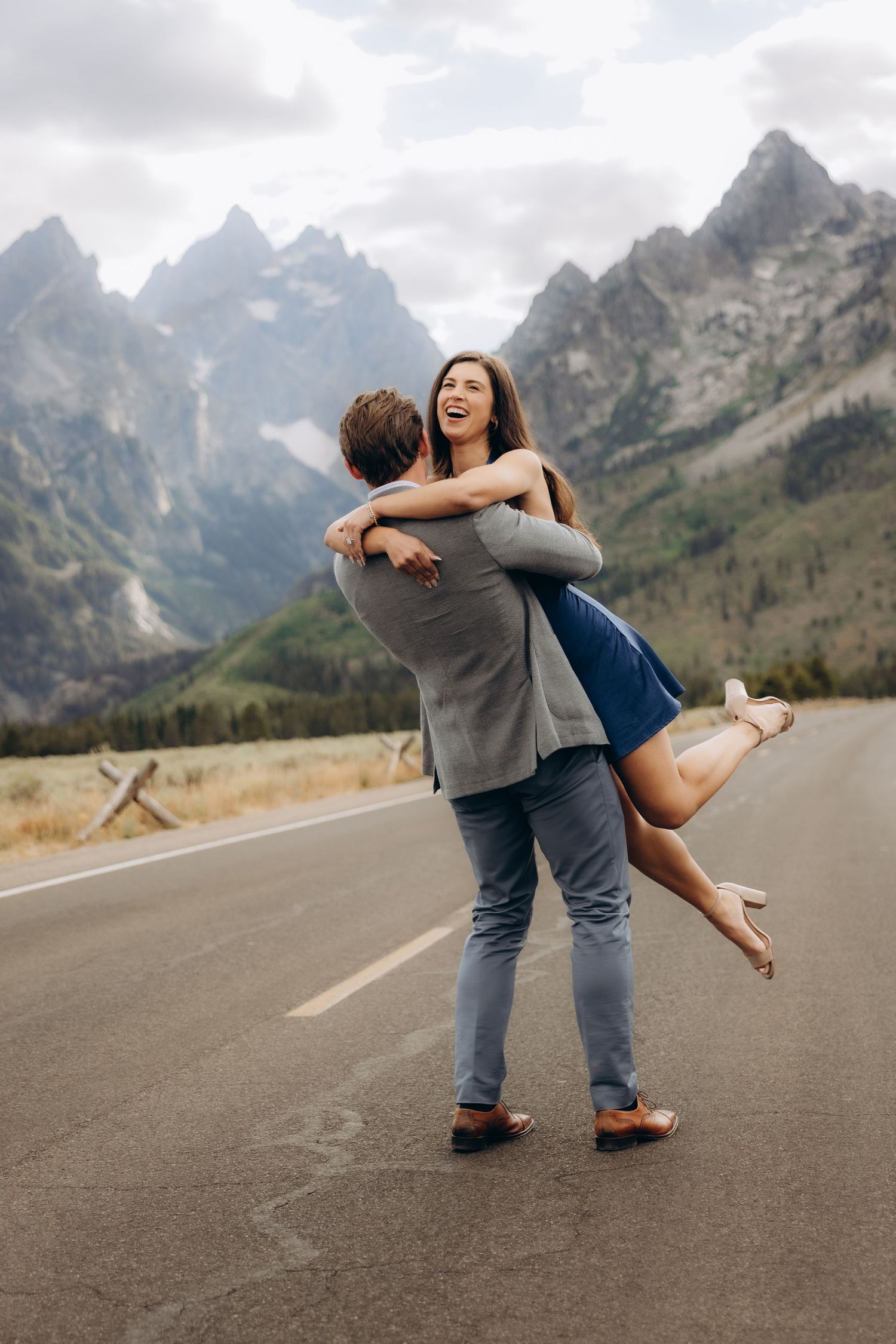 A couple shares a romantic dance pose on a scenic mountain road with dramatic peaks in the background.