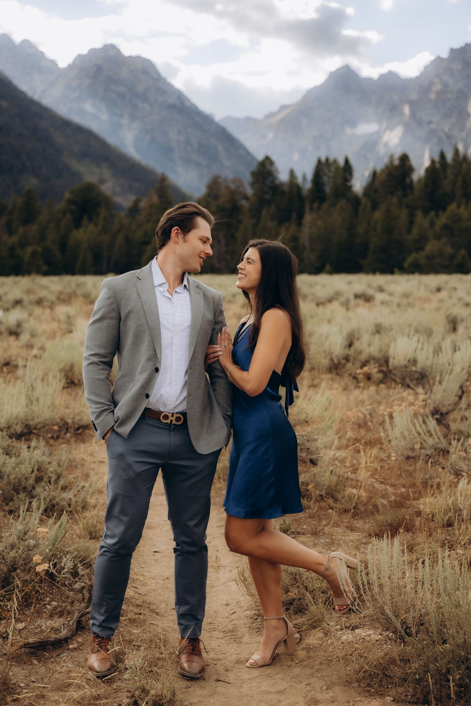 A couple shares an intimate moment in front of rugged mountain peaks during a golden hour photoshoot.