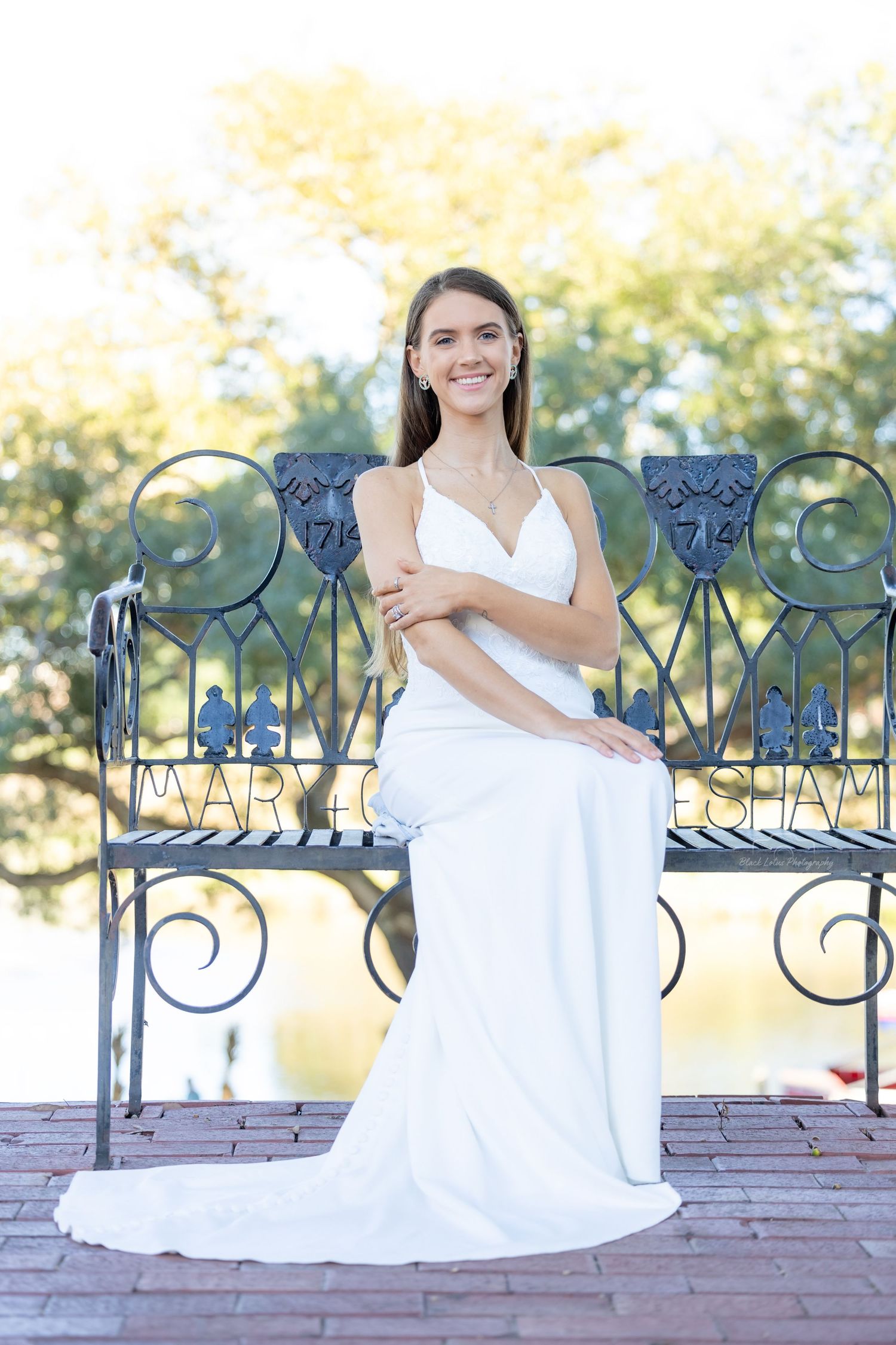 Person in white dress sitting and posing on decorative wrought iron bench against autumn outdoor backdrop.