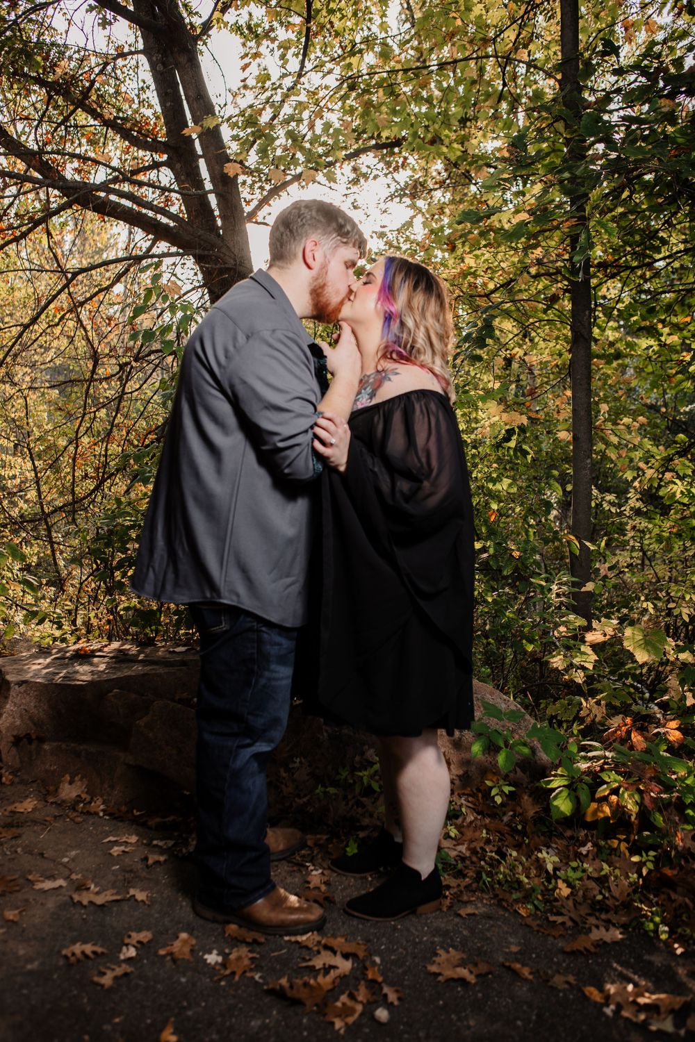 Romantic couple poses under fall foliage in a wooded outdoor setting.