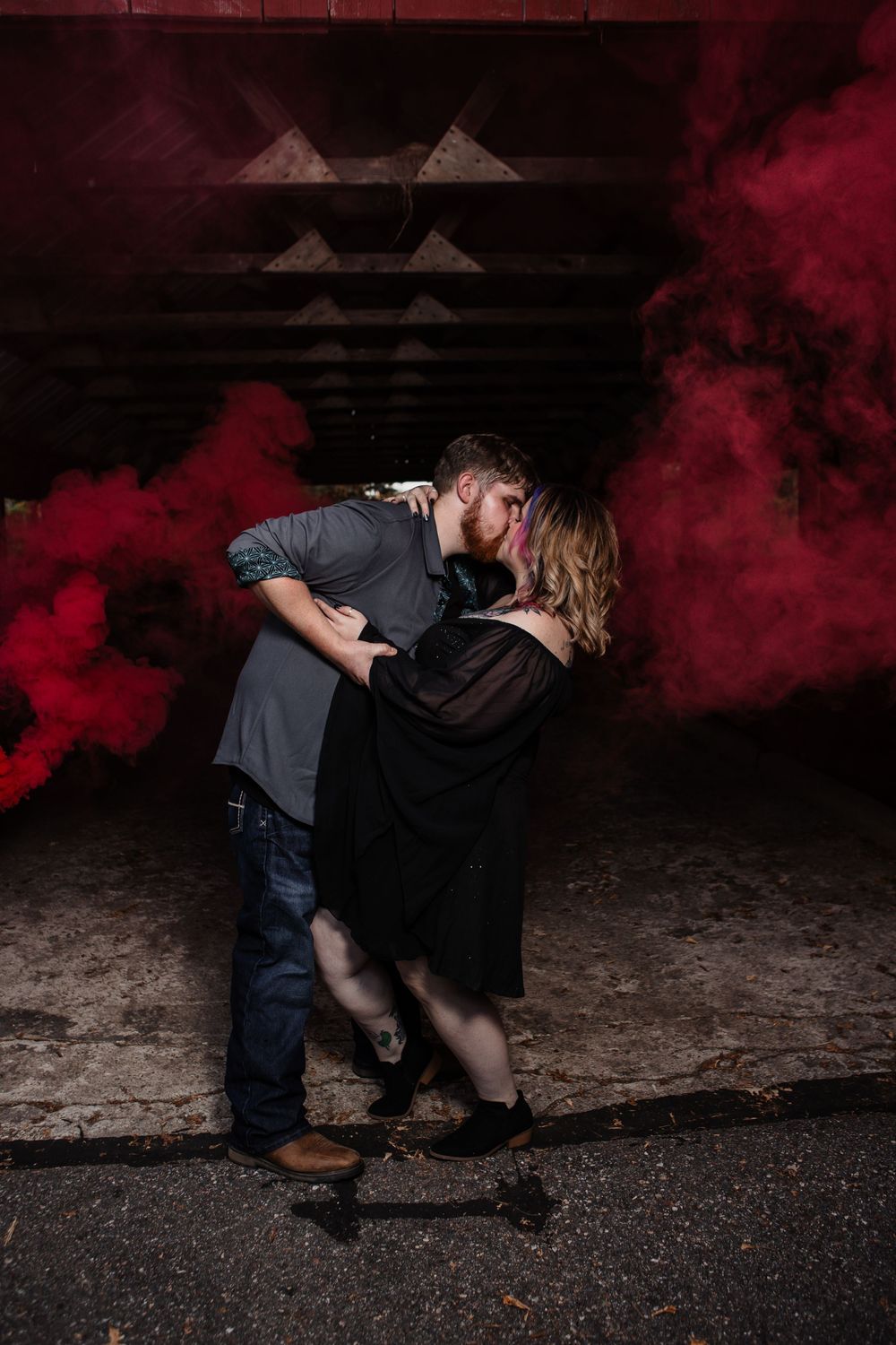 Couple in dramatic pose with red smoke effects in dark outdoor setting.