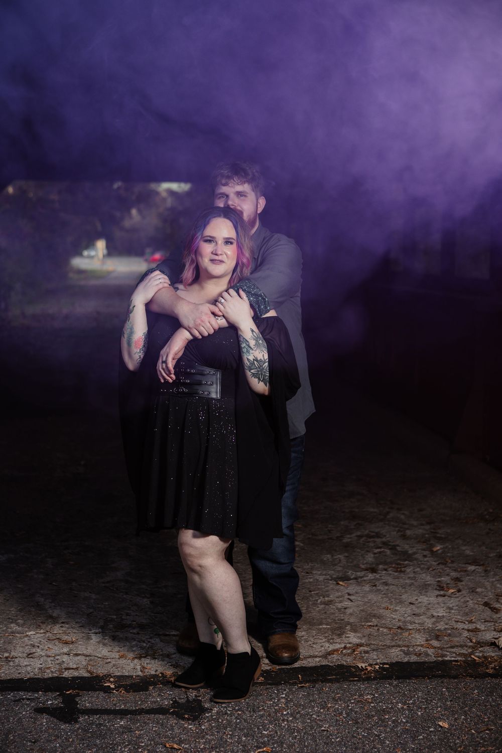 Couple embracing in artistic portrait with purple smoke effects at night.