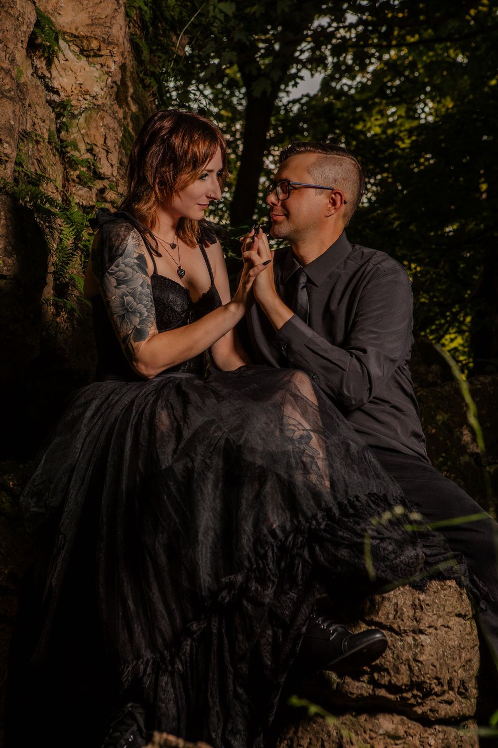 A couple in dark formal wear shares tender moments against a rocky outdoor setting.