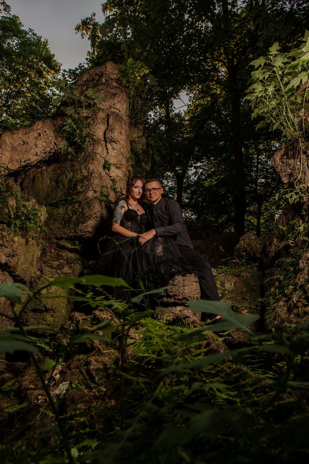 A couple shares intimate moments on rocky terrain surrounded by lush forest vegetation.