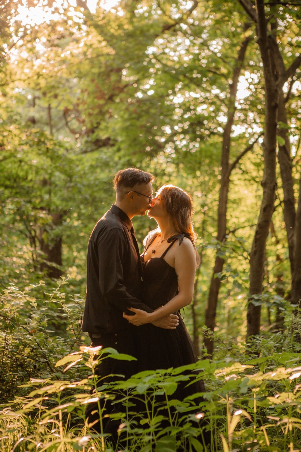 A romantic couple embraces in a sunlit forest setting with golden light filtering through trees.