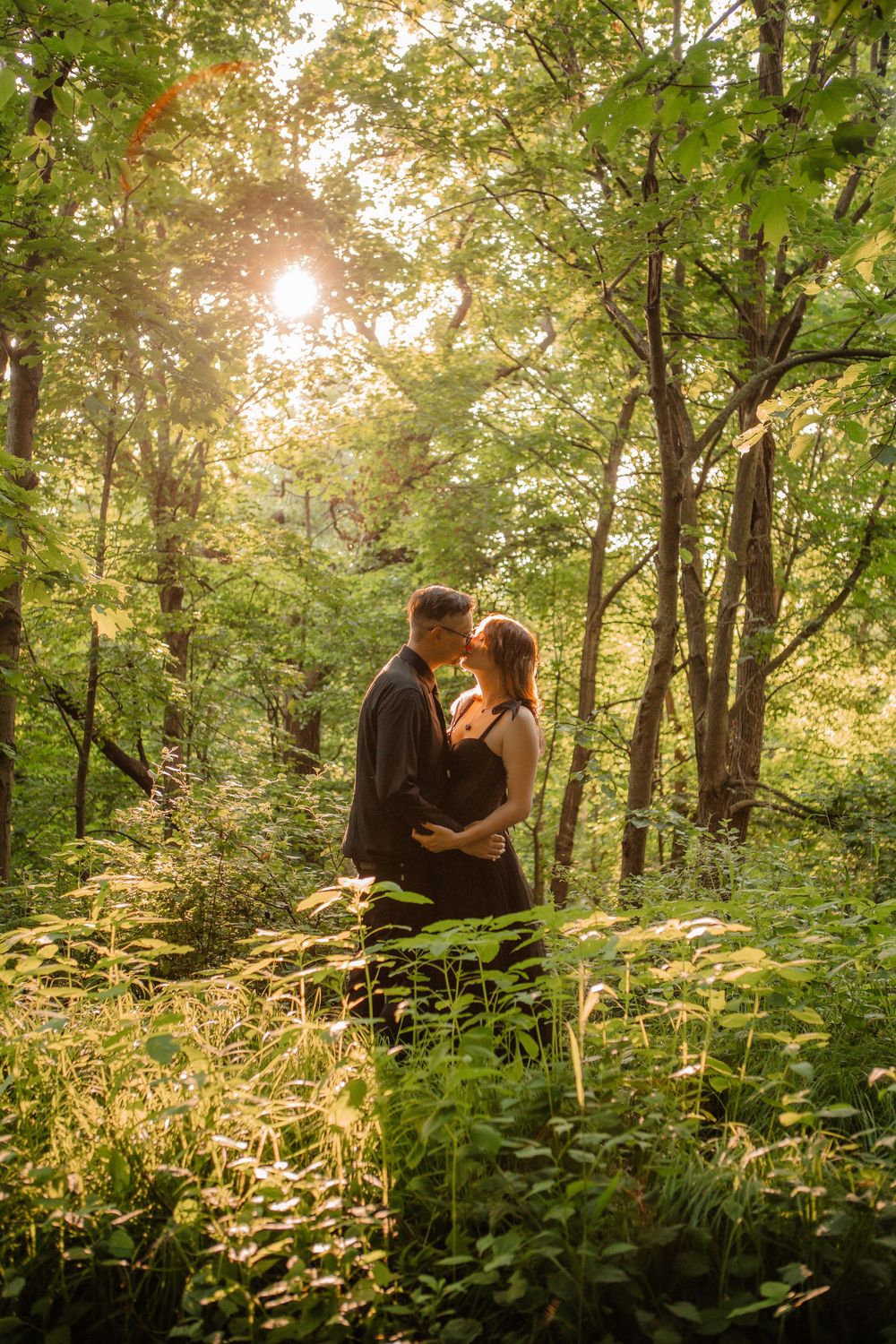 A couple shares an intimate moment in a sunlit forest with glowing vegetation.