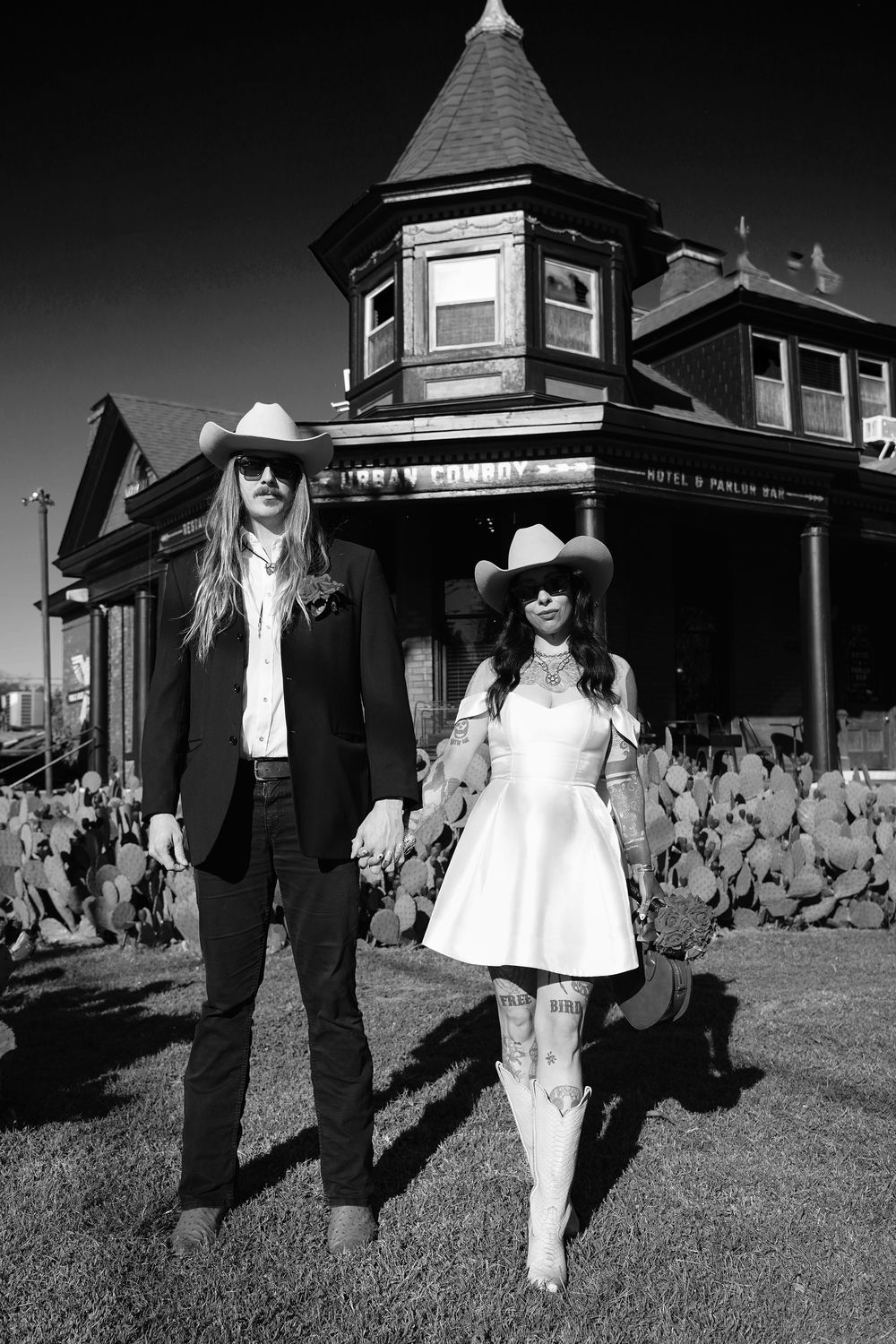 Black and white photo of people in western wear walking past vintage buildings.