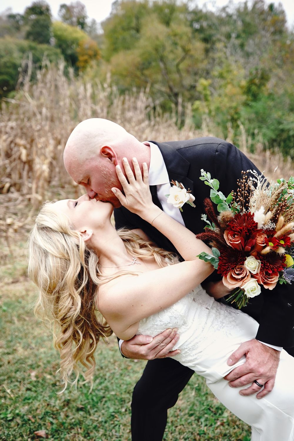 Romantic dip pose with autumn floral bouquet during outdoor wedding photoshoot.