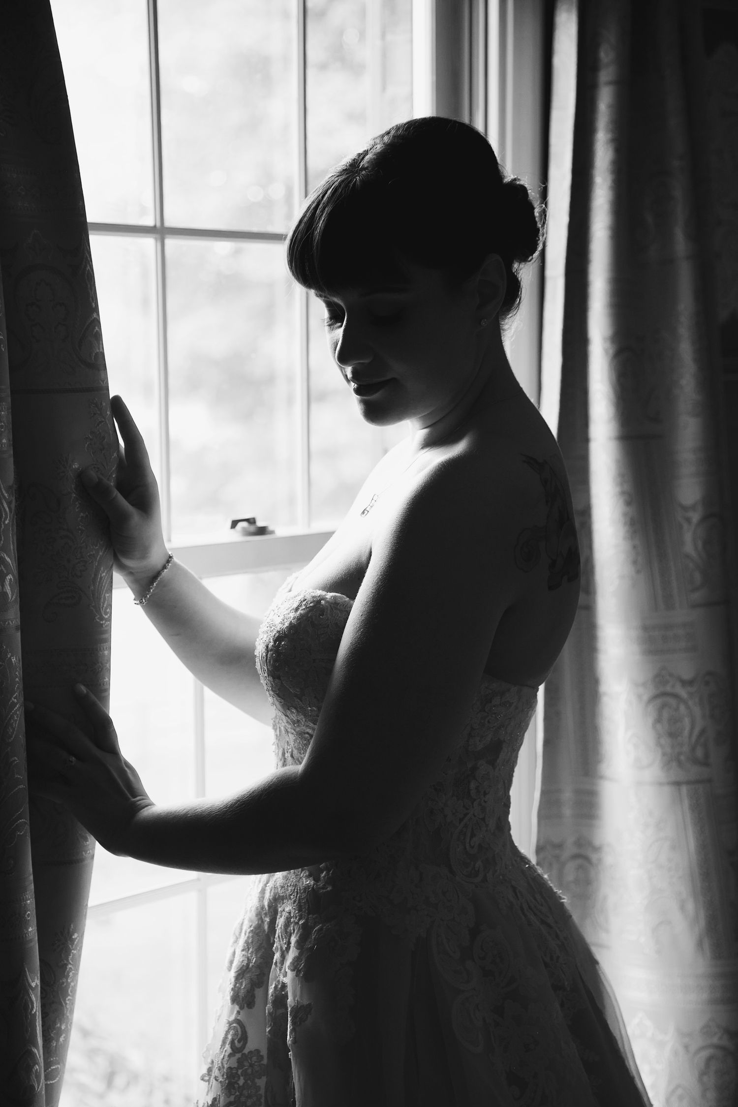 Silhouette of a bride in a wedding dress standing by a window with flowing curtains.
