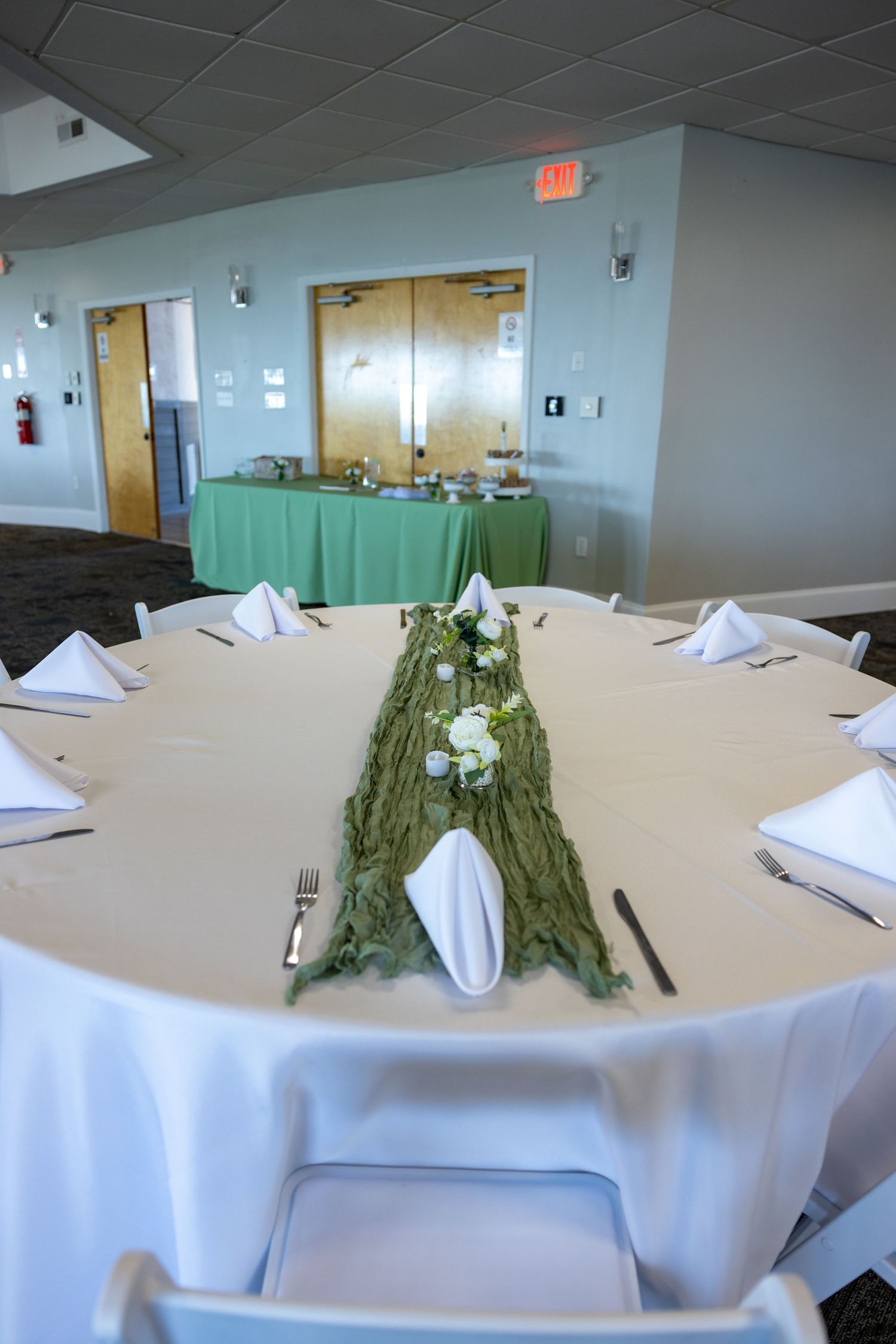 Round banquet tables with white tablecloths and palm frond centerpieces arranged in an indoor event space.