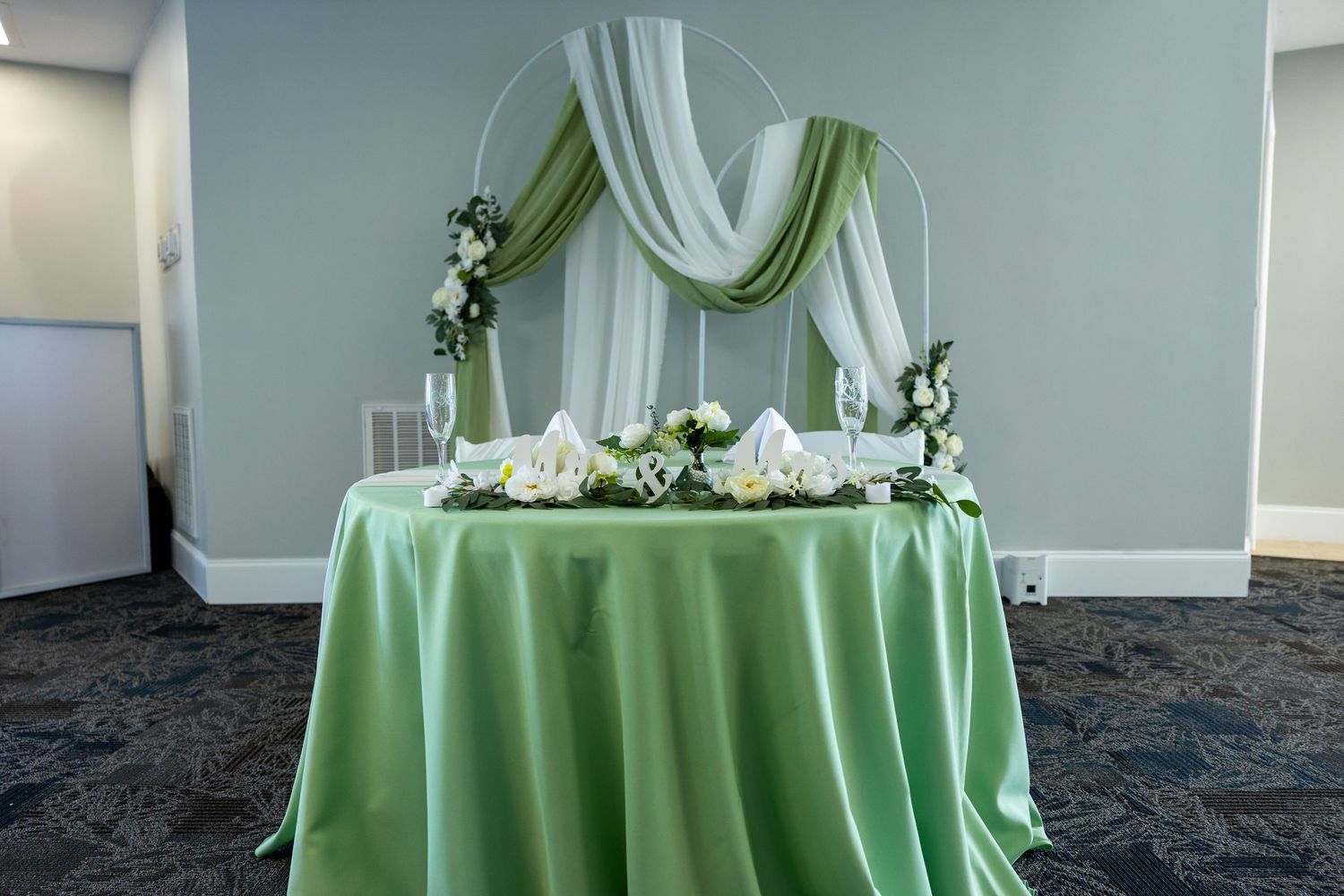 Elegant sweetheart table with mint green tablecloth and white fabric draping adorned with floral arrangements.