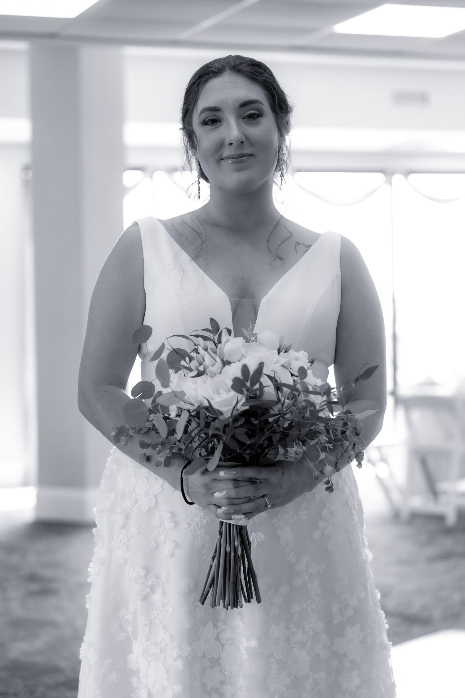 Black and white portrait of a bride in a lace wedding dress holding a bouquet of flowers.