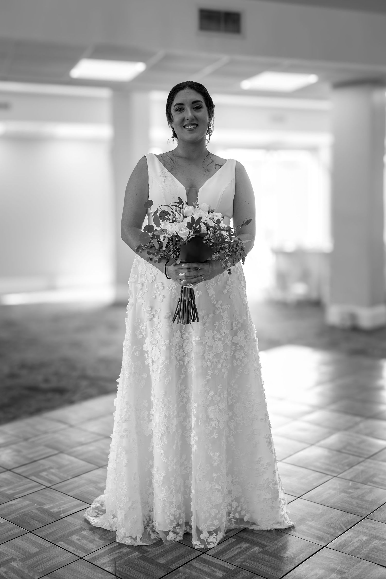 A white lace wedding dress elegantly displayed on a tiled floor in an indoor venue.