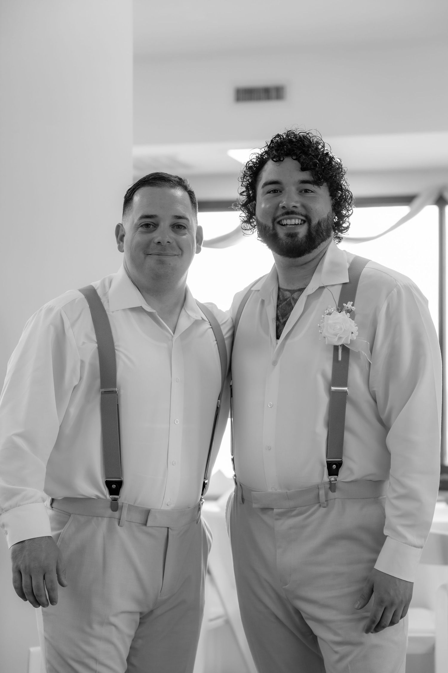 Wedding party members in white shirts and gray suspenders pose together indoors.